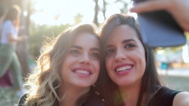 Female friends posing together taking selfie with cellphone outdoors