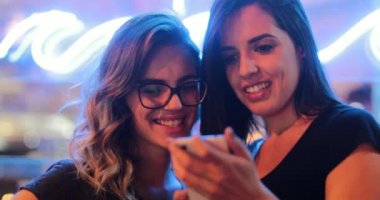 Two young women holding cellphone at night checking media content online