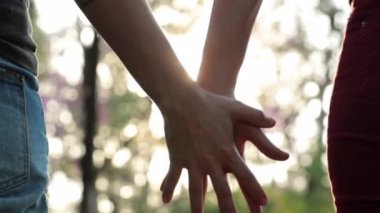 Close-up of couple holding hands together at the park with sunlight flare in the background