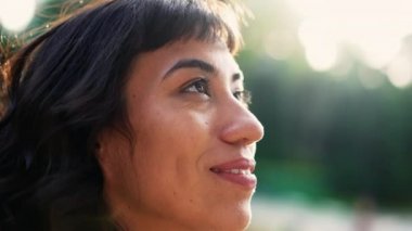 Happy South American young woman looking at sky smiling with HOPE standing outside in SUNLIGHT
