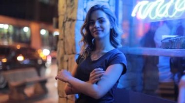 Woman crossing arms next to neon sign in city streets outside