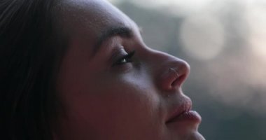 Young woman face opening and closing eyes. Girl meditating and in contemplation looking up to the sky with hope and faith