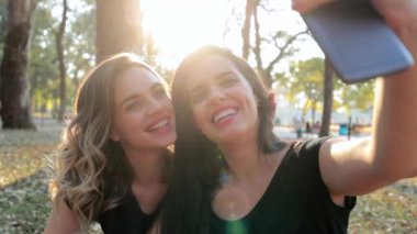 LGBT lesbian couple posing together taking selfie with cellphone outdoors with lens flare