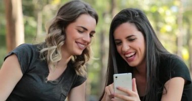 Authentic friends together outdoors checking cellphone. Girls looking and holding smartphone chatting exchanging gossip