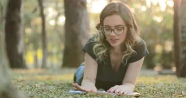 Girl lying on grass outside at the park wiping cleaning book surface