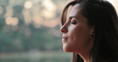 Young woman with eyes closed taking a deep breath outside at the park