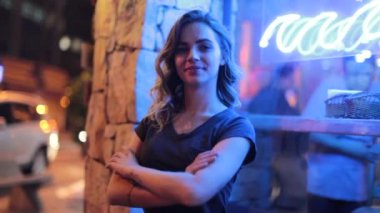 Woman crossing arms next to neon sign in city streets outside