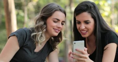 Authentic friends together outdoors checking cellphone. Girls looking and holding smartphone chatting exchanging gossip