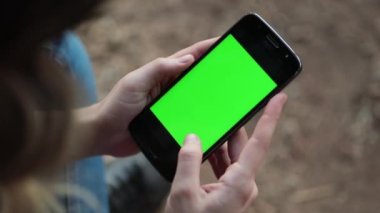 Person holding cellphone with green screen. Woman looking at smartphone with green-screen