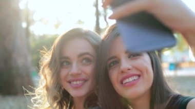 Female friends posing together taking selfie with cellphone outdoors