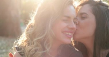 Girlfriends posing for selfie, friend kissing female partner in cheek, candid authentic real life gay couple