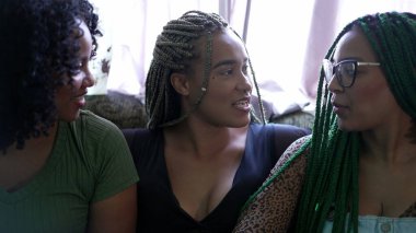 Three hispanic black women sitting on couch laughing and smiling together