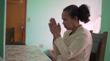 Contemplative senior person praying at home. One hopeful older black lady in meditation prayer
