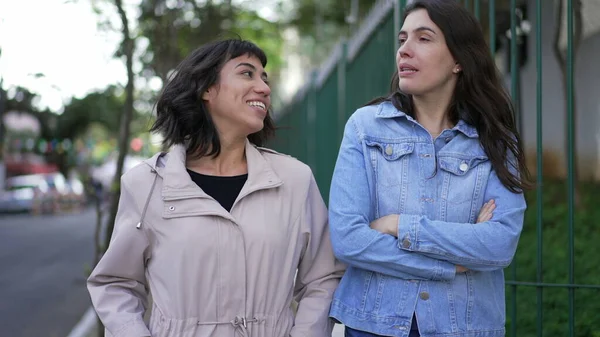 Two women in conversation walking in city street. Female friends talking