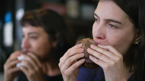 Two people eating burgers. Young women taking a bite of cheeseburgers. Female friends eating fast food lunch