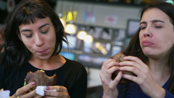 Two Happy Young Women Eating Cheeseburgers Restaurant Girlfriends Taking Bite — Foto de Stock