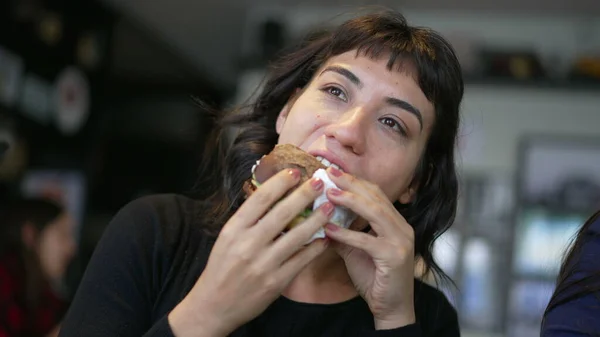 One hispanic woman eating burger. A latin american girl eats fast food cheeseburger