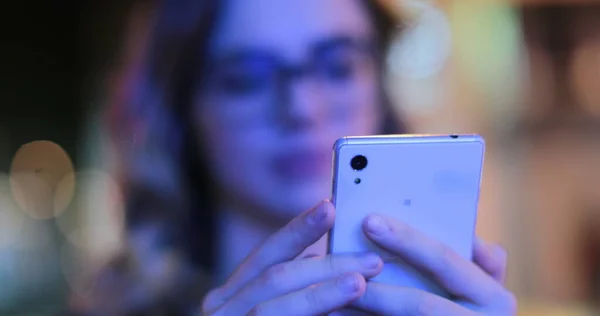 Girl wearing glasses checking cellphone at night in city atmosphere