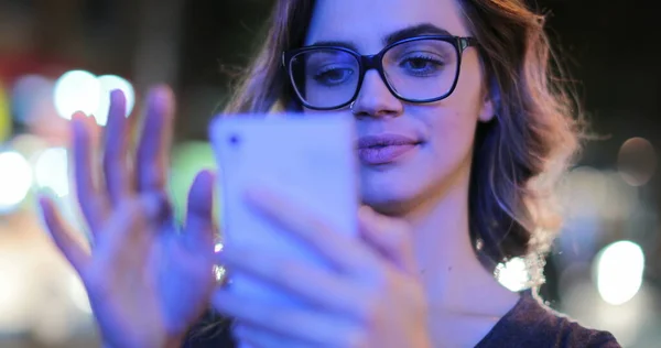 Girl wearing glasses checking cellphone at night in city atmosphere