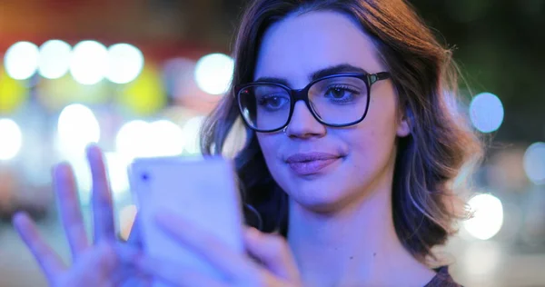 Girl wearing glasses checking cellphone at night in city atmosphere