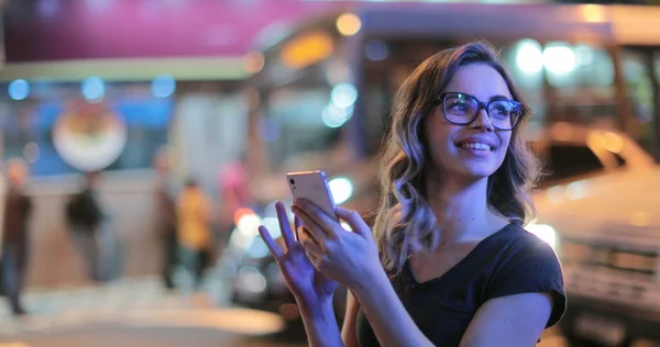 Girl holding cellphone screen at night outside at the city. Young woman checking smartphone in the evening night-life