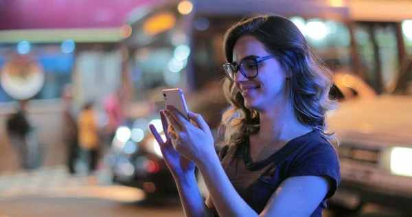 Girl holding cellphone screen at night outside at the city. Young woman checking smartphone in the evening night-life