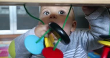 Cute baby boy playing with arch toy at home putting in mouth