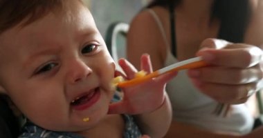 Mother feeding upset crying baby boy in highchair