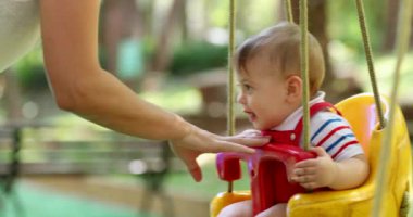 Happy baby boy toddler at playground park swing mom pushing son at swing
