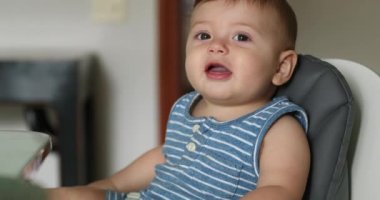 Cute baby infant toddler seated at highchair looking to camera smiling