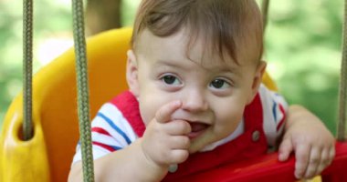 Closeup of smiling happy baby infant boy at playground park swing