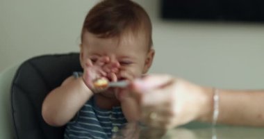Mother trying to feed upset baby son toddler