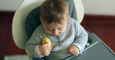Vertical shot of baby infant dropping piece of apple fruit on the floor