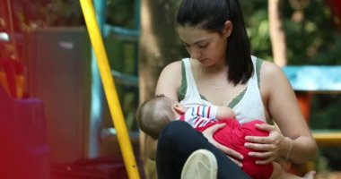 Casual candid mother breastfeeding baby son outside at park