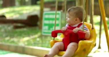 Joyful baby boy toddler at playground swing at park