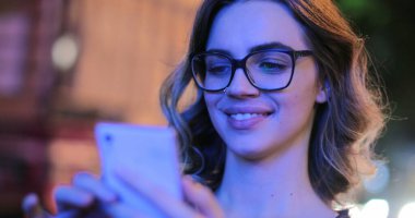 Young woman holding smartphone in the evening next to moving traffic