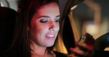 Passenger young woman checking and holding her cellphone while riding taxi at night