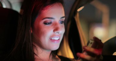 Passenger young woman checking and holding her cellphone while riding taxi at night