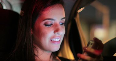 Passenger young woman checking and holding her cellphone while riding taxi at night