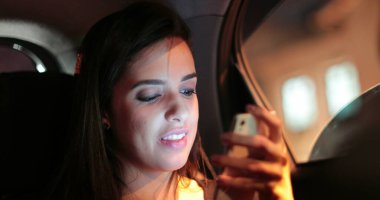 Passenger young woman checking and holding her cellphone while riding taxi at night