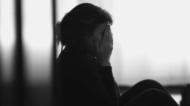 Monochromatic shot of desperate young woman suffering from emotional pain sitting on floor at home