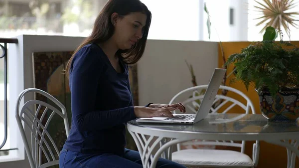 Young woman working from home in front of laptop computer at apartment balcony terrace