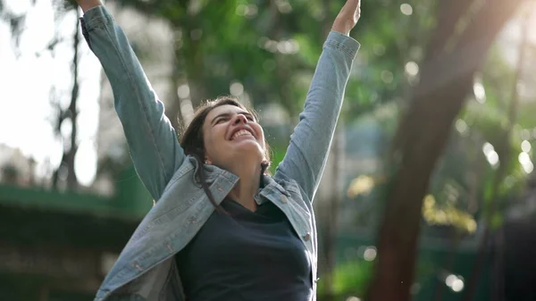 Happy woman celebrating achievement raising arms in the air feeling FREEDOM. Joyful person standing outside in nature