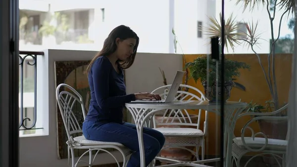 Young woman working from home in front of laptop computer at apartment balcony terrace
