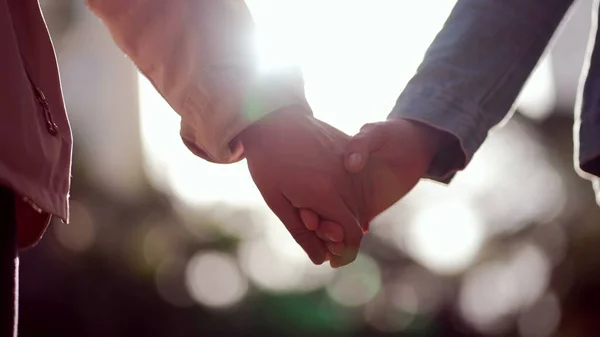 Hands joining together with sunlight flare in the background. Beautiful friendship moment between two people