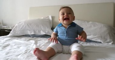 Happy adorable baby seated on bed at home, casual and authentic