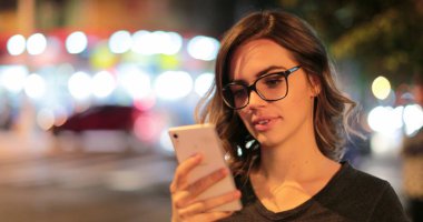 Young woman checking her cellphone at night Latina girl holding her smartphone