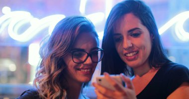 Two young women holding cellphone at night checking media content online