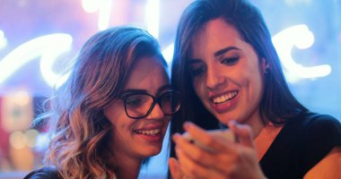 Two young women holding cellphone at night checking media content online