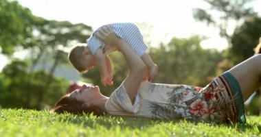 Mom holding baby in the air outdoors during golden hour sunset